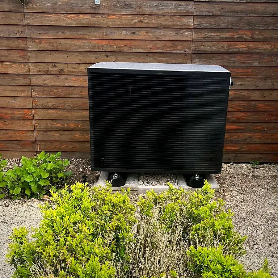 Air-to-water heat pump on a concrete base in front of a wooden fence, in Versoix